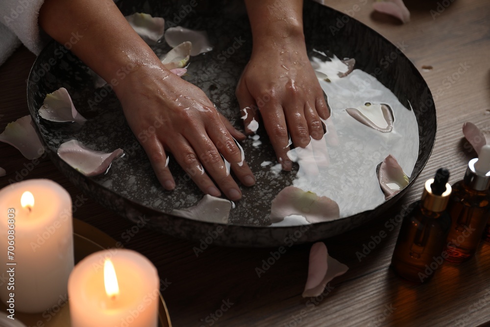 Fototapeta premium Woman soaking her hands in bowl of water and flower petals at table, closeup. Spa treatment
