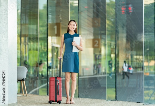 Business woman with suitcase, holding a laptop getting a ride to the airport