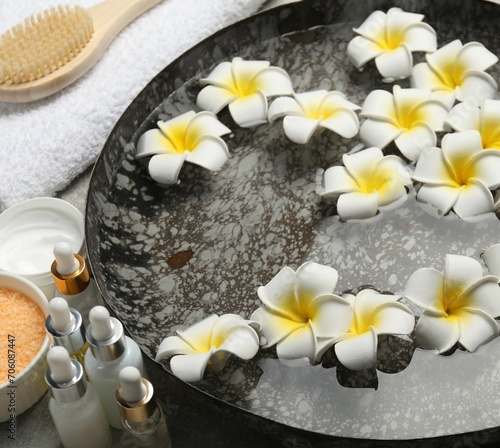 Bowl of water with flowers and different spa supplies on table