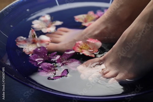 Woman soaking her feet in bowl with water and flowers, closeup. Spa treatment