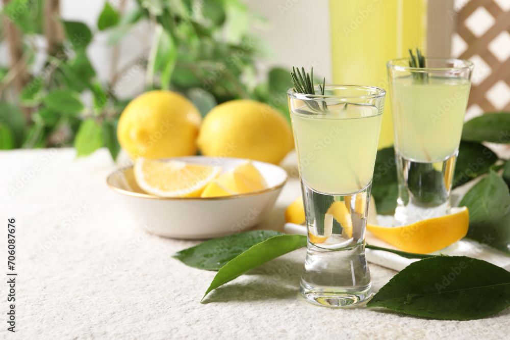Tasty limoncello liqueur, lemons and green leaves on white textured table, closeup. Space for text
