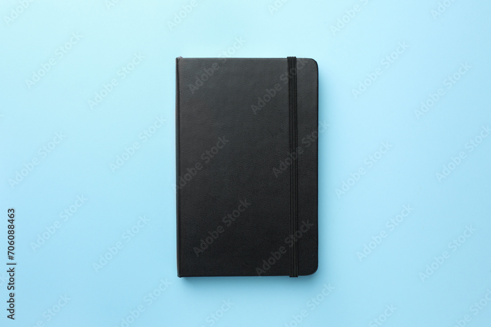 Closed black notebook on light blue background, top view Closed black notebook on light blue background, top view