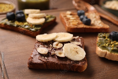 Toasts with different nut butters, banana slices, blueberries and nuts on wooden board, closeup