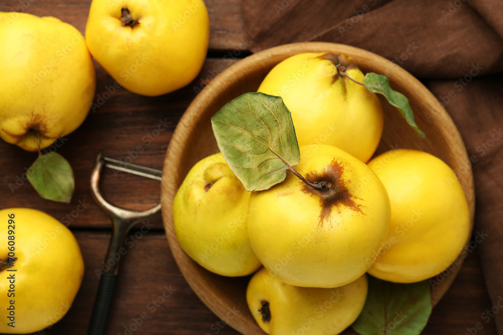 Tasty ripe quince fruits in bowl and peeler on wooden table, flat lay