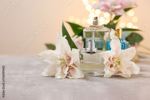 Bottles of perfume and beautiful lily flowers on table against beige background with blurred lights, closeup. Space for text