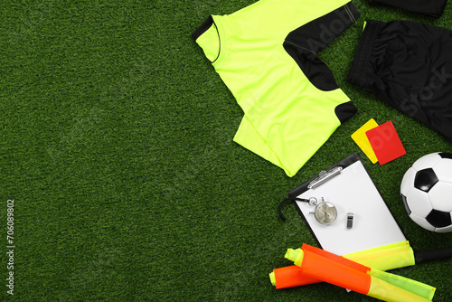 Uniform, soccer ball and other referee equipment on green grass, flat lay. Space for text photo