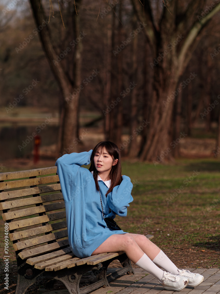 Fototapeta premium Beautiful young Chinese woman posing in sunny summer forest, wearing blue loose oversized top and miniskirt with small shoulder bag. Emotions, people, beauty, youth and lifestyle portrait.