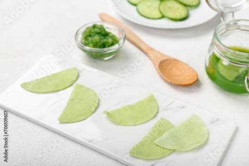 Board with cotton under-eye patches made of cucumber on white table, closeup