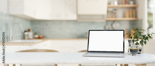 Home workspace, a white-screen laptop computer on a white dining table in a modern bright kitchen.