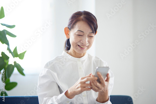 リビングにてスマートフォンを使用する日本人のシニア女性