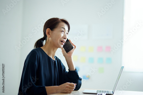 オフィスにてスマートフォンで電話をする日本人シニア女性 photo