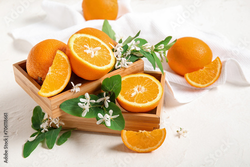 Wooden box of oranges with blooming branch on white table