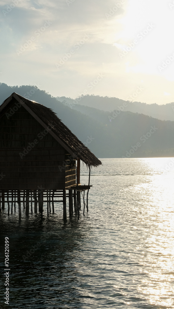 Solo traditional wooden thatched roof hut overlooking ocean with golden sunlight on tropical island in Raja Ampat, West Papua, Indonesia Solo traditional wooden thatched roof hut overlooking ocean with golden sunlight on tropical island in Raja Ampat, West Papua, Indonesia