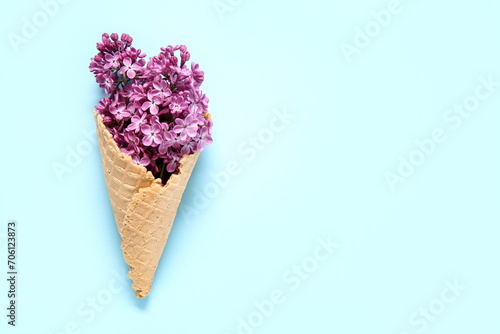 Waffle cone with beautiful lilac flowers on blue background