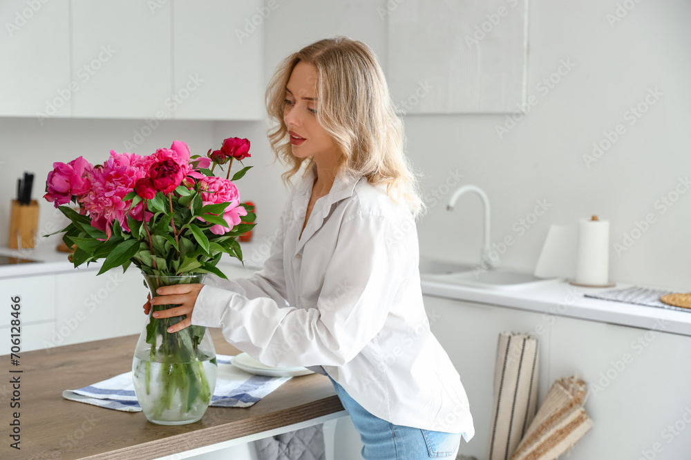 Young woman and vase with peony flowers in kitchen Young woman and vase with peony flowers in kitchen