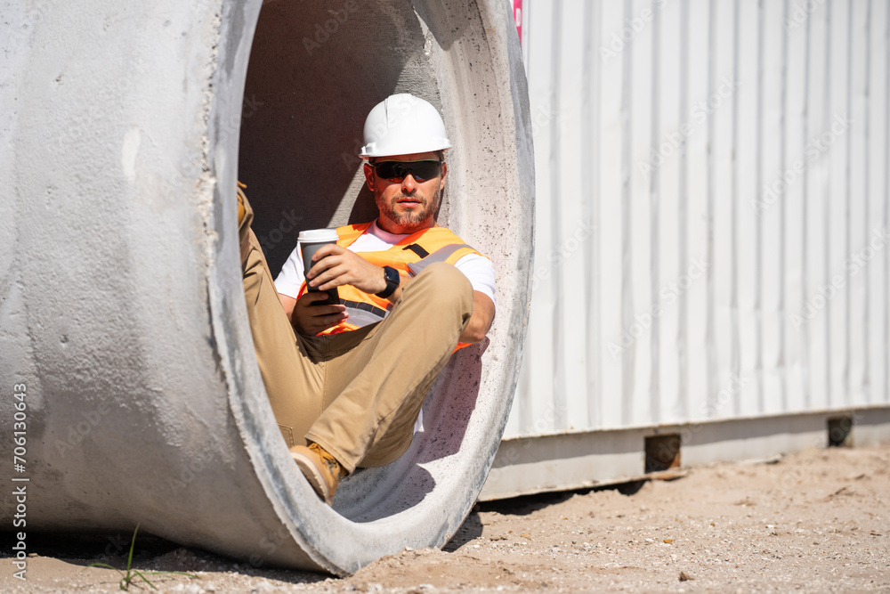 Coffee, engineer and construction worker relax on break at construction site. handsome male builder in hard hat smiling at camera. Construction Worker on Duty. Contractor and the Wooden House Frame Coffee, engineer and construction worker relax on break at construction site. handsome male builder in hard hat smiling at camera. Construction Worker on Duty. Contractor and the Wooden House Frame