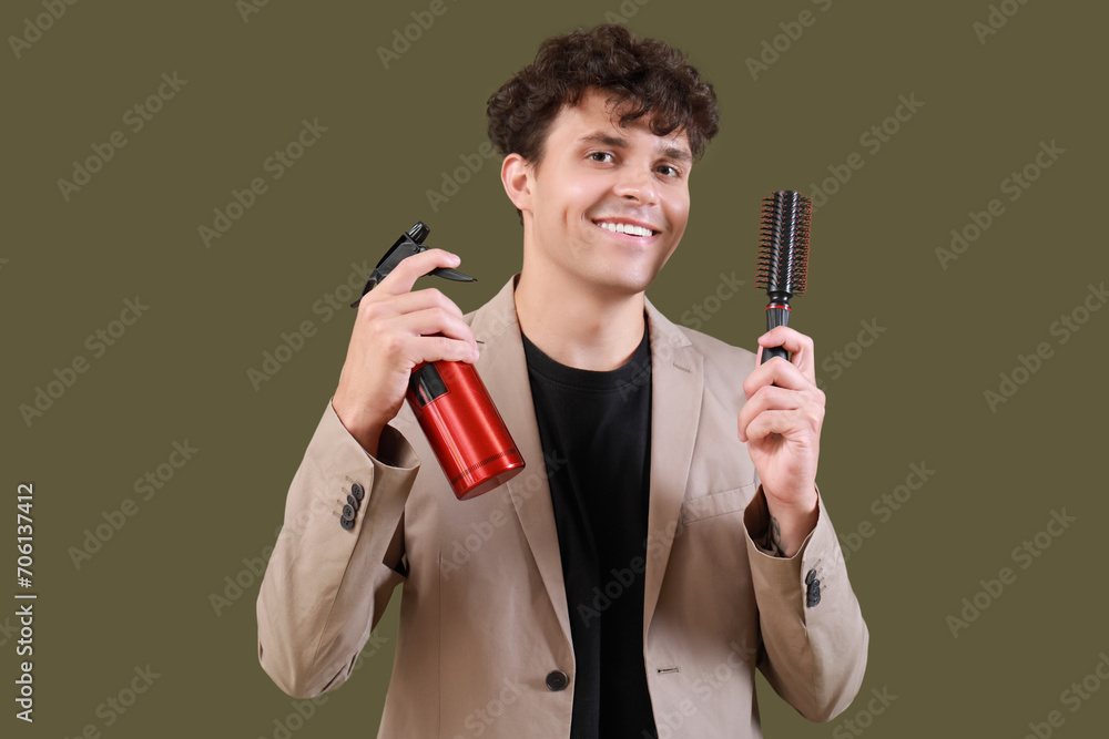 Handsome young man with bottle of hair spray and brush on green background Handsome young man with bottle of hair spray and brush on green background