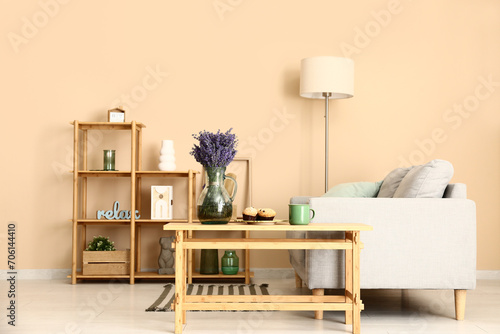 Interior of stylish living room with shelving unit, sofa, lamp, table and beautiful lavender flowers