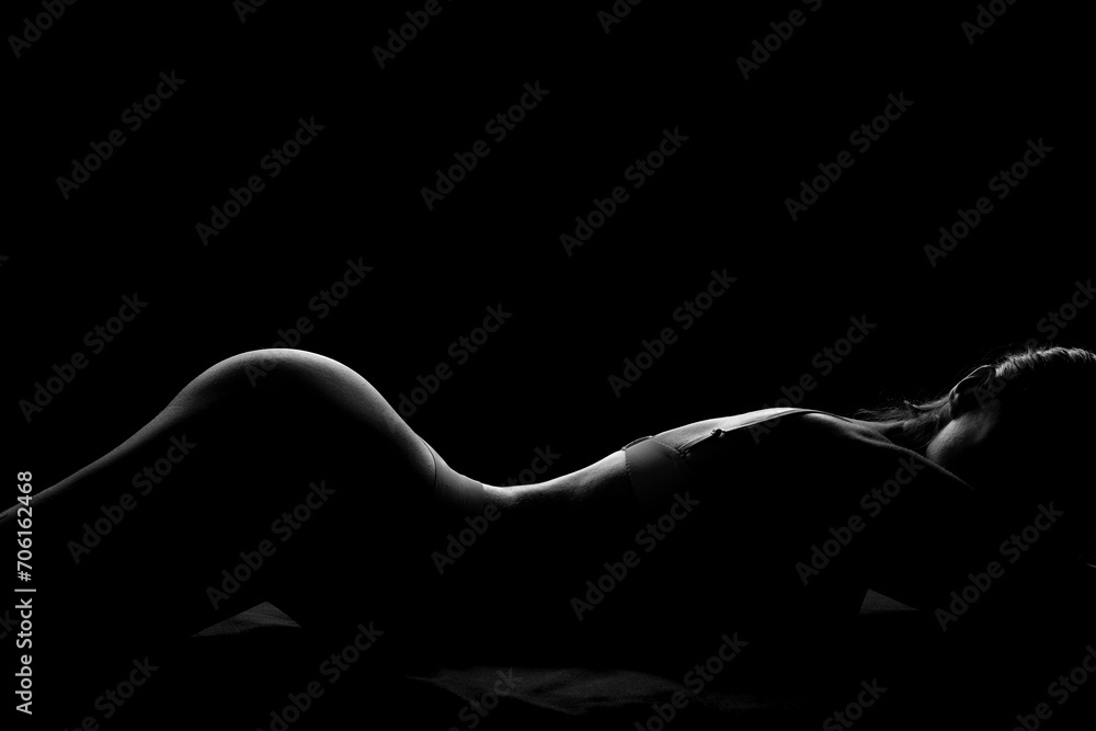 Silhouette of attractive young woman in underwear lying on dark background - obrazy, fototapety, plakaty 