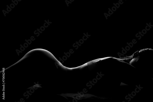 Silhouette of attractive young woman in underwear lying on dark background photo