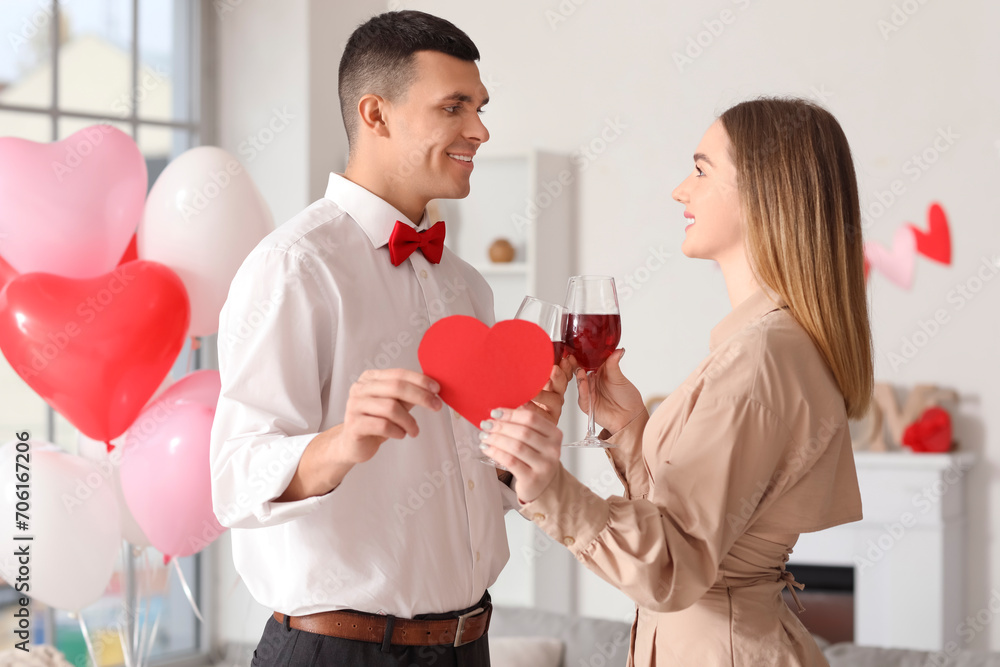 Beautiful young couple with paper heart and glasses of wine celebrating Valentine's Day at home Beautiful young couple with paper heart and glasses of wine celebrating Valentine's Day at home