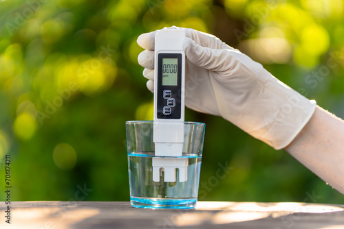 Foto pH meter in hands with gloves, glass of water on blurred background of nature