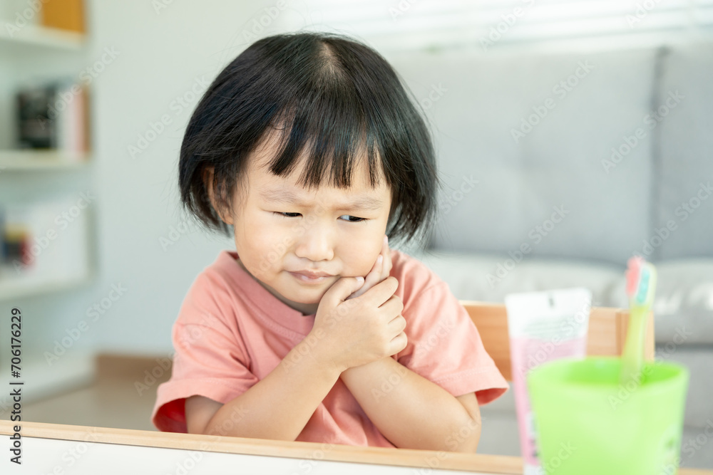 little asian girl presses hand to cheek, suffers from pain in tooth. Teeth decay, dental problems, child emotions and facial expression, oral health care, reducing sweets, fluorine coating little asian girl presses hand to cheek, suffers from pain in tooth. Teeth decay, dental problems, child emotions and facial expression, oral health care, reducing sweets, fluorine coating