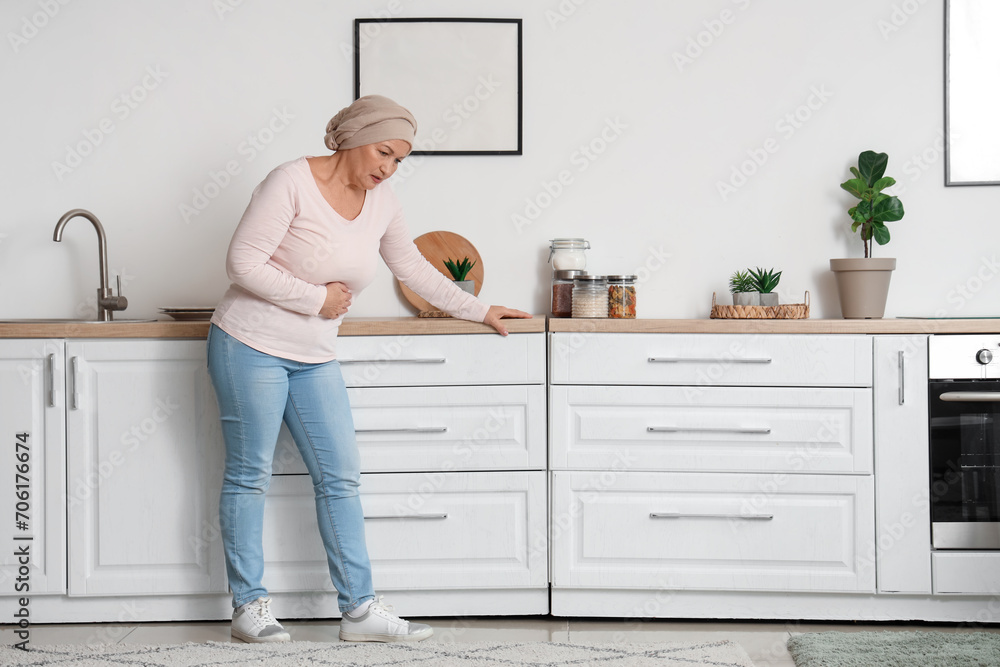 Mature woman after chemotherapy suffering from pain in kitchen. Stomach cancer concept Mature woman after chemotherapy suffering from pain in kitchen. Stomach cancer concept