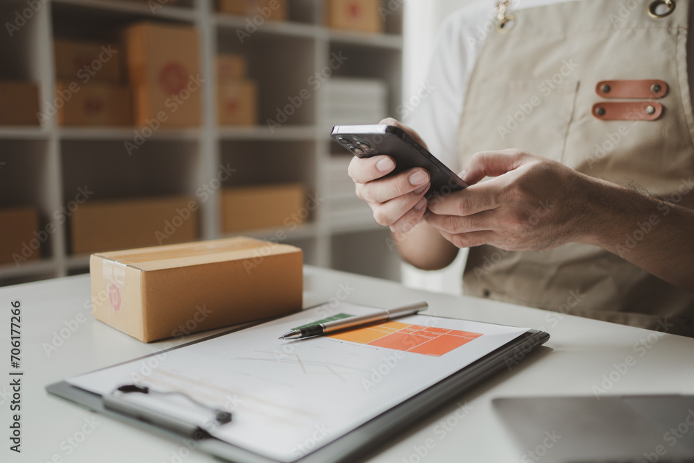 Fototapeta premium Smartphones are being used to do various activities to promote sales to stores, owner of an online store packs products into parcel boxes based on orders from online sales sites.