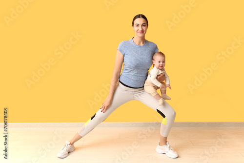 Beautiful young sporty woman with her little baby practicing yoga near yellow wall