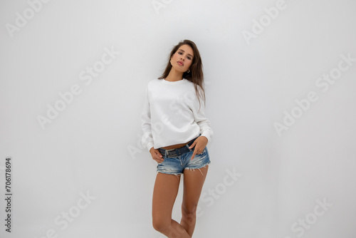 Beautiful girl in shorts and a white sweatshirt posing on a white background