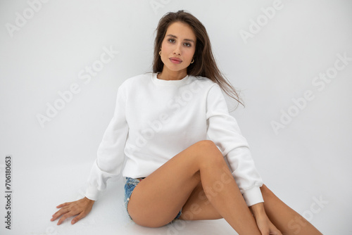 Beautiful girl in shorts and a white sweatshirt posing on a white background