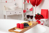 Bathtub tray with candles, fruits and glasses of wine in bathroom. Valentine's Day celebration