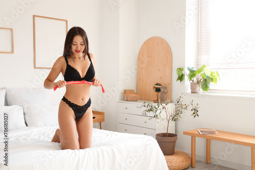 Sexy young Asian woman with whip in bedroom. Valentine's Day celebration