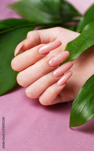 Female hands with pink nail design  hold green leaves