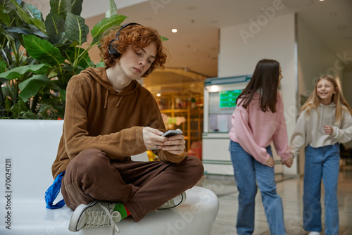 Upset teenage guy sitting alone while his friends walking in shopping mall photo