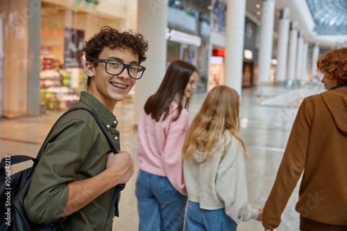 Portrait of happy teenage by turning his back while walking with friends at mall