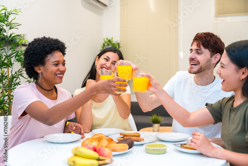 Multi-ethnic friends toasting with orange juice having breakfast at home