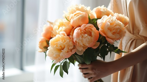 Fototapeta Naklejka Na Ścianę i Meble -  Women's hands holding a bouquet of peach peonies for congratulations on Mother's Day, Valentine's Day, women's Day. Blurred background.