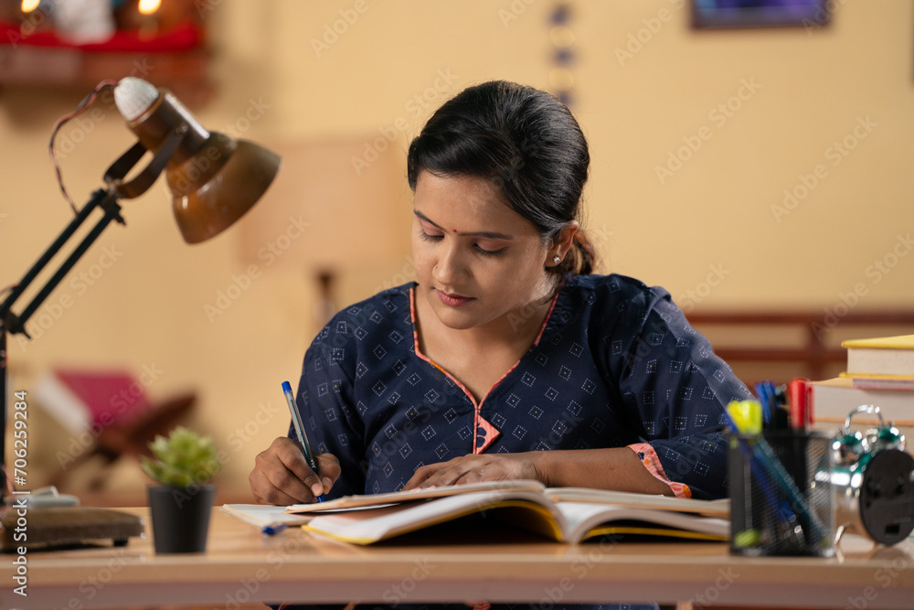 Indian young teenager girl using mobile phone for studying at home - concept of exam preparation, internet and technology - obrazy, fototapety, plakaty 