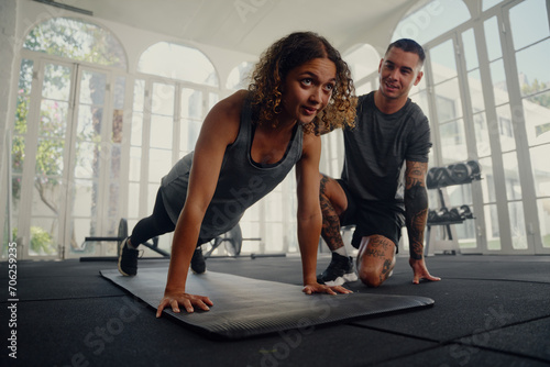 Multiracial trainer with young woman in sports clothing doing push-up exercises at the gym