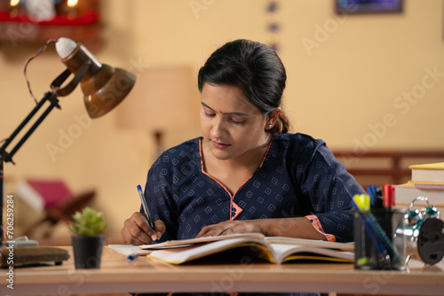 Indian young teenager girl using mobile phone for studying at home - concept of exam preparation, internet and technology photo