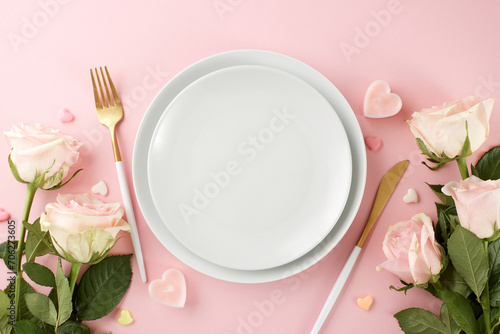 Commemorative Valentine's Day dining occasion. Top view composition of plates, cutlery, hearts, roses on pastel pink background