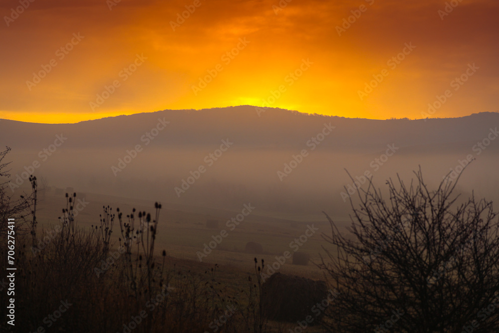 Obraz premium Autumn foggy sunrise. Sunrise photo with a landscape covered in fog, amazing orange sky in the country side.