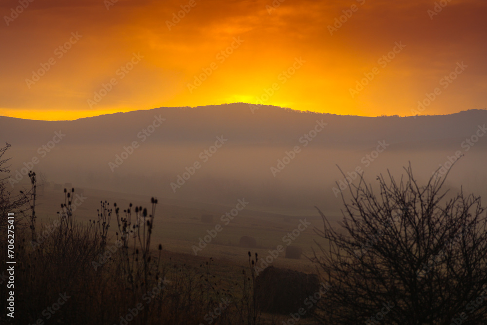 Autumn foggy sunrise. Sunrise photo with a landscape covered in fog, amazing orange sky in the country side.