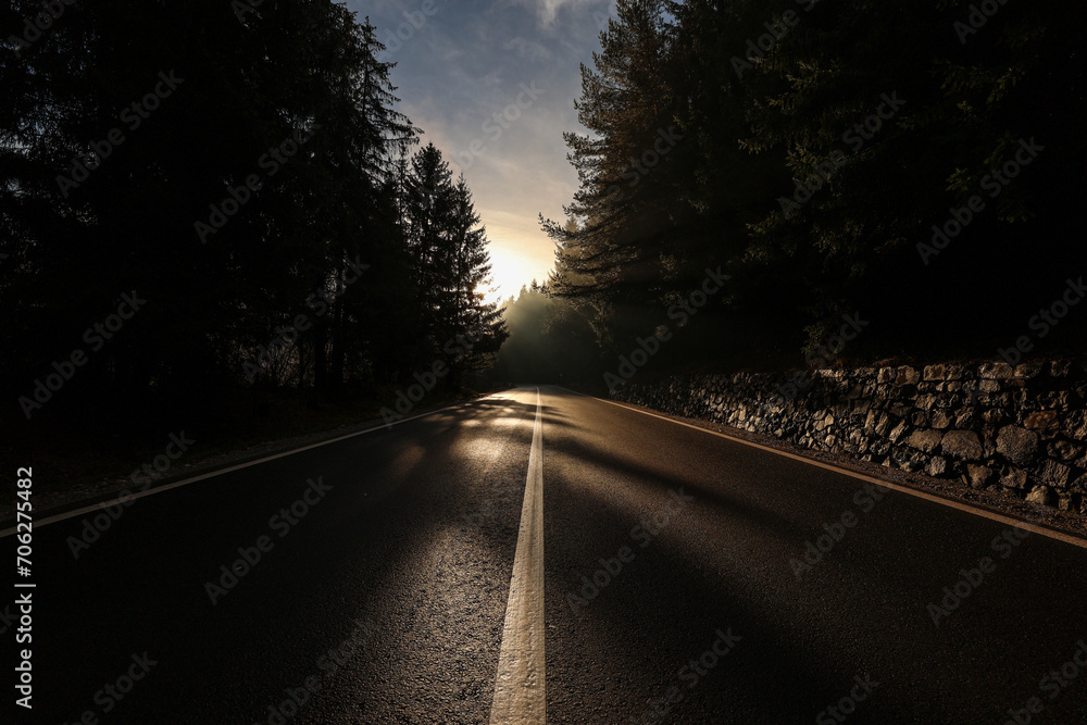 Amazing road in the mountain forest. Rays of sun bursting through the tree branches of this beautiful curved road in the morning. Transportation industry.