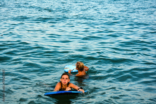 Two children with a swimming board in the water, girl cheekily sticks out her tongue photo