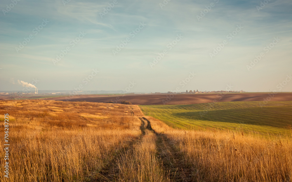 Trail in the dry meadow. Vanishing point track in hilly countryside field on sunset. Shortcut via unpaved road in grasslands.