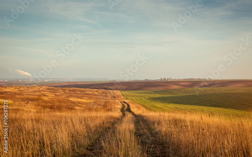 Trail in the dry meadow. Vanishing point track in hilly countryside field on sunset. Shortcut via unpaved road in grasslands.