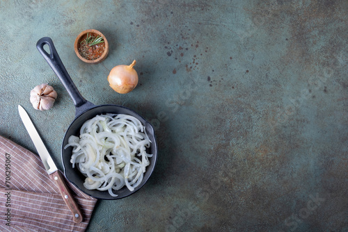 A frying pan with chopped onions standing on a linen napkin on a dark surface.